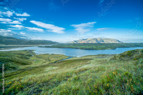 Landscape photography of a mountain in Iceland having smooth running river in foreground with green autumn grass meadow