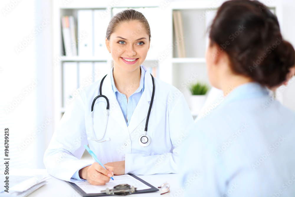 Friendly smiling doctor and patient sitting at the table Friendly smiling doctor and patient sitting at the table