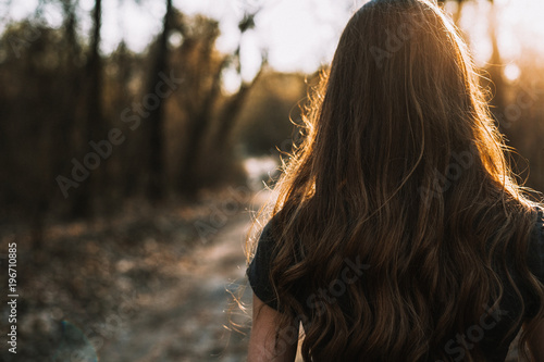 Rear view of sad young woman walking through park at sunset