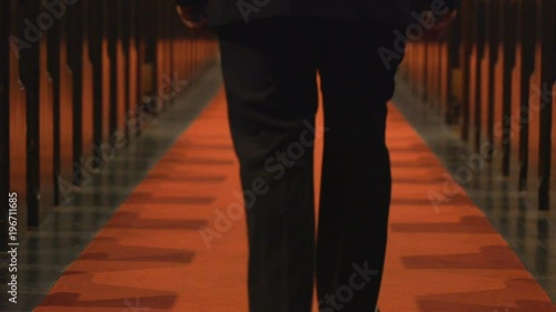 Man walks down aisle between church pews, low shot