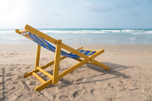 An yellow beach chair rests on the white sand of the beach and Bright blue sea with white clouds  at Rayong Thailand.