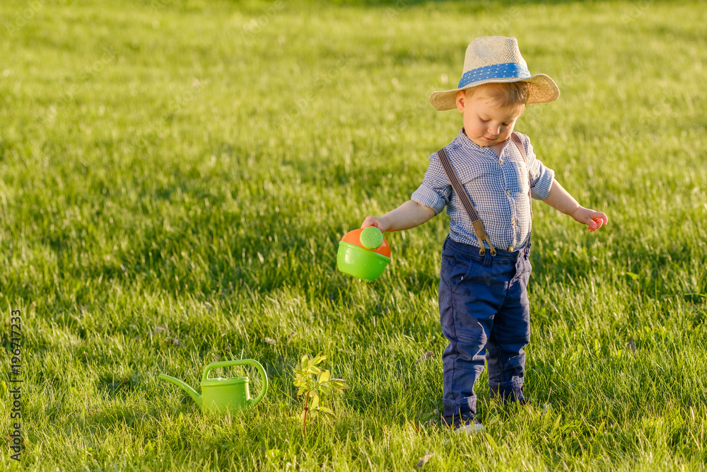 Toddler child outdoors. One year old baby boy wearing straw hat using watering can Toddler child outdoors. One year old baby boy wearing straw hat using watering can