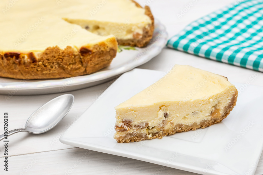 Piece of cheesecake on saucer with whole cheesecake and kitchen towel on the table. Piece of cheesecake on saucer with whole cheesecake and kitchen towel on the table.