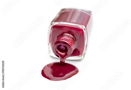 Red nail polish spilled from the bottle on white background.