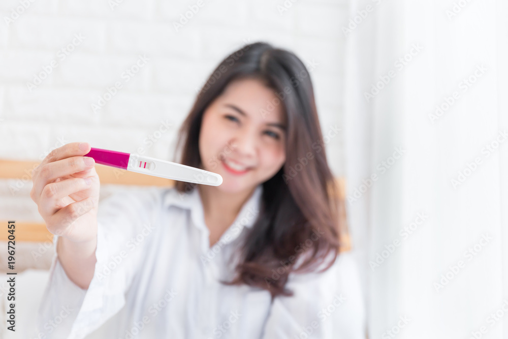 Selective focus Pregnancy test positive result on hand of smiling woman in her bedroom,Blurred background. Selective focus Pregnancy test positive result on hand of smiling woman in her bedroom,Blurred background.