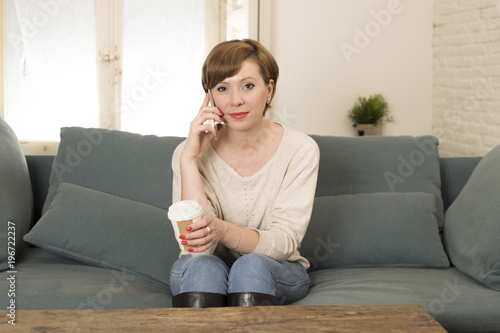 young attractive and happy red hair woman sitting at home sofa couch drinking coffee talking on mobile phone relaxed in communication concept