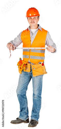 builder in a helmet holding tape-measure in his hands and looking at camera