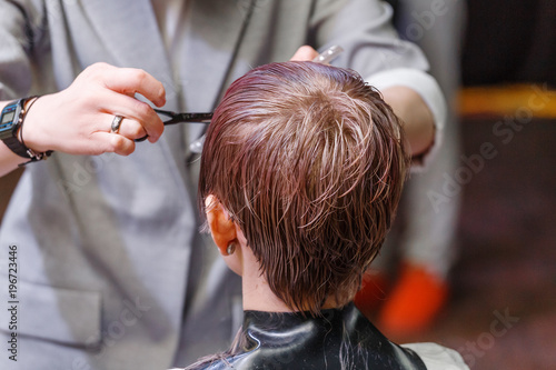 Close up hairdresser's hands cutting client's hair by scissors of young woman in beauty salon