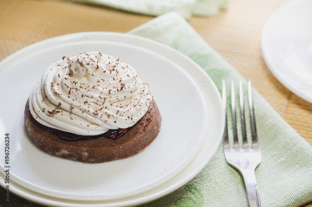 A chocolate cake with egg white cream on a white plate and fork, located on a green serviette A chocolate cake with egg white cream on a white plate and fork, located on a green serviette