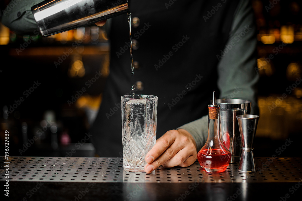 Barman puring a fresh alcoholic drink from shakerinto a glass