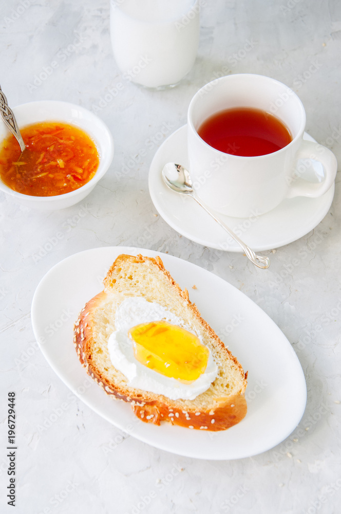 Slice of homemade challah bread with jam, glass of milk and a cup of tea on a white background. Breakfast concept.