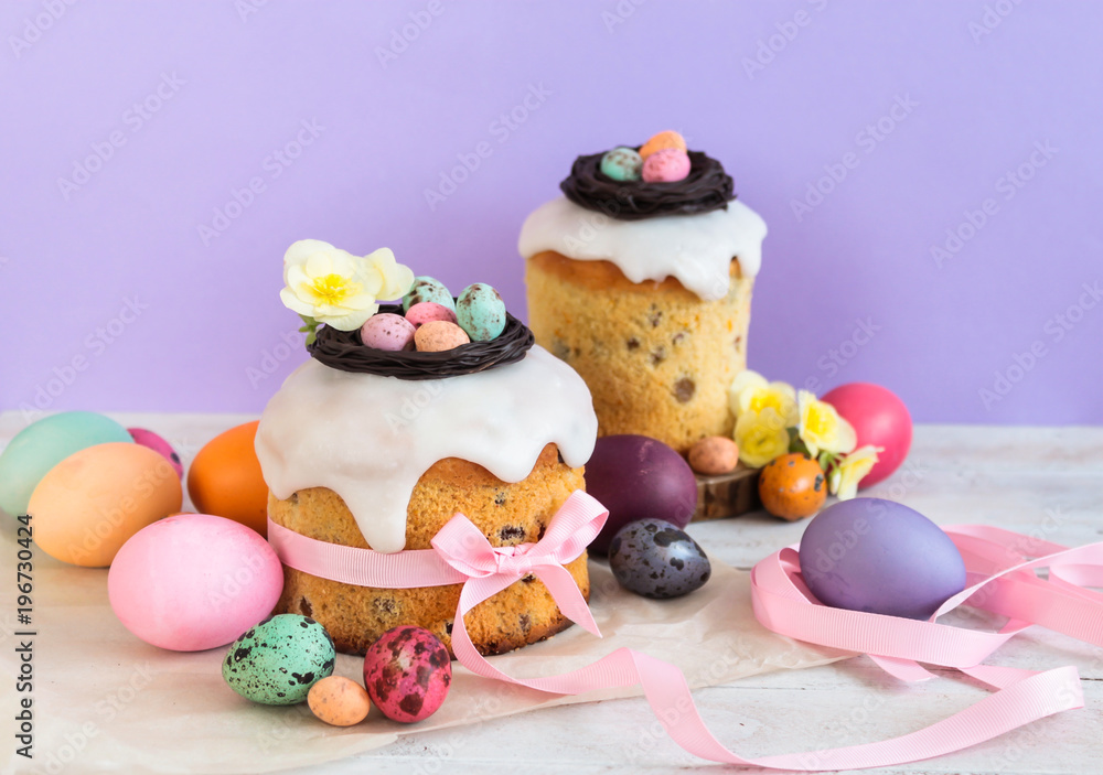 Obraz premium Colorful Easter spring stillife in soft light and trendy pastel colors. Traditional cake with chocolate nest, candy and qail eggs decoration blossom flowers on violet background