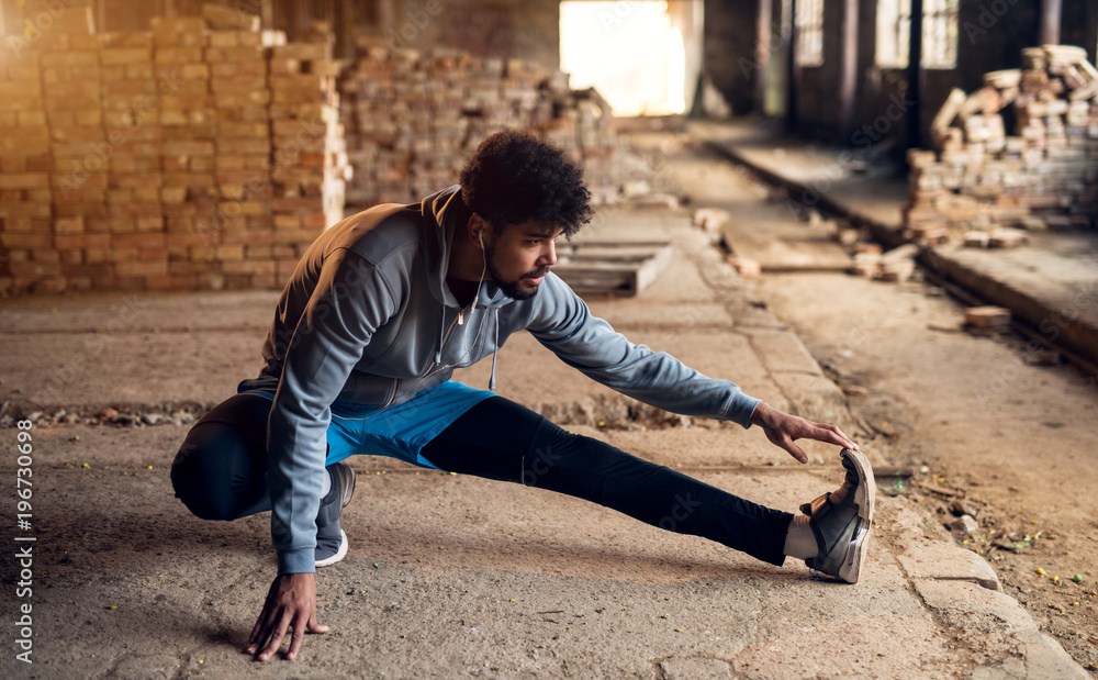 Close up portrait of active afro-american young attractive athletic man doing full leg stretching workout inside of the abandoned place. Close up portrait of active afro-american young attractive athletic man doing full leg stretching workout inside of the abandoned place.