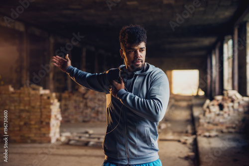 Close up portrait of active afro-american young attractive athletic man doing full hand stretching workout inside of the abandoned place. photo