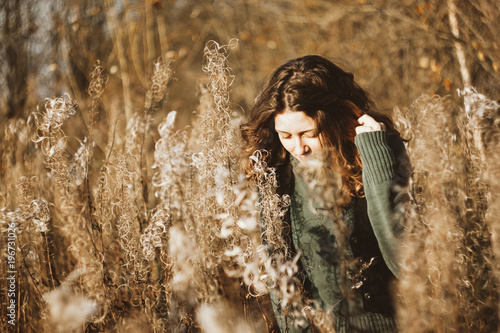 Girl is standing in the tall grass in the autumn at sunset