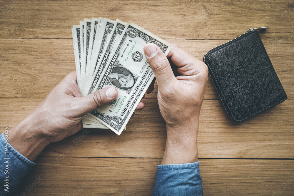 Male hand holing money dollar bill with wallet on wood table.business investment Male hand holing money dollar bill with wallet on wood table.business investment