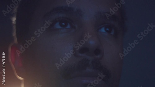 upset boring mixed race man watching tv in darkness with different color light from tv on face. Eyes closeup