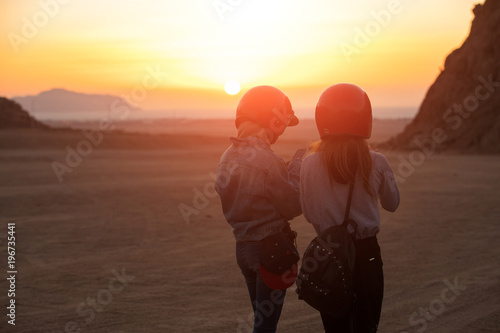 Women tourists with helmet, morning sunrise in desert, rear view, looking smartphone