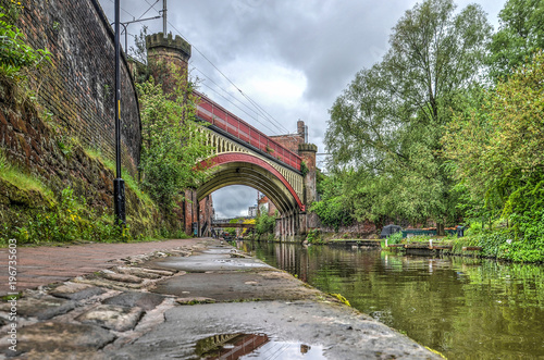 View from the footpath along Rochdale canal in the Castlefield area in the center of Manchester, England towards a historic steel railway bridge photo