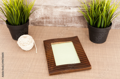 Beautiful photo frame lying on table next to two pots of grass