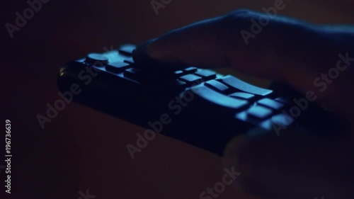 closeup of tv controller and man's hand pushing buttons in screenlight