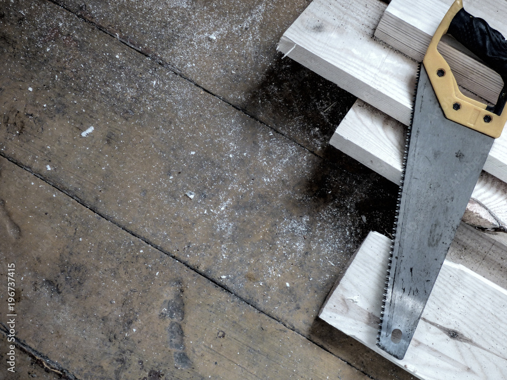 New fresh boards and saw on aged wooden surface (floor or table). Abstract background. Natural materials - two kinds of wood. Filtered, desaturated. New fresh boards and saw on aged wooden surface (floor or table). Abstract background. Natural materials - two kinds of wood. Filtered, desaturated.