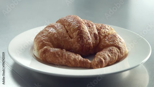 closeup of inox table and man's hand putting a dish with croissant on it in morning light