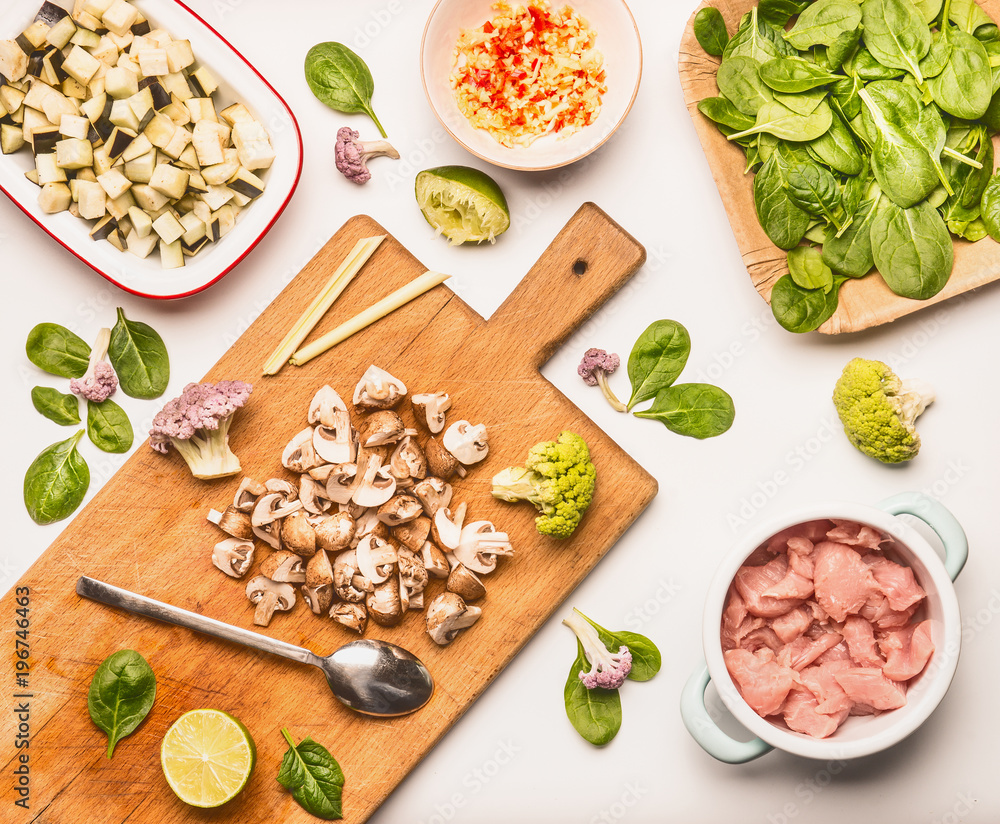 Food flat lay with spinach, chicken meat , chopped champignon and eggplant, lemon and vegetables on cutting board with cooking spoon on white background, top view Food flat lay with spinach, chicken meat , chopped champignon and eggplant, lemon and vegetables on cutting board with cooking spoon on white background, top view