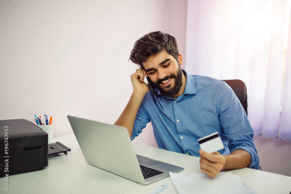 Confident young businessman shopping online on a laptop in the office. Confident young businessman shopping online on a laptop in the office.