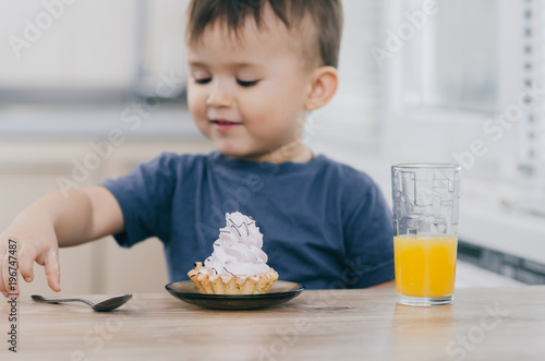 the child in the kitchen takes a spoon  going to eat a beautiful white cake