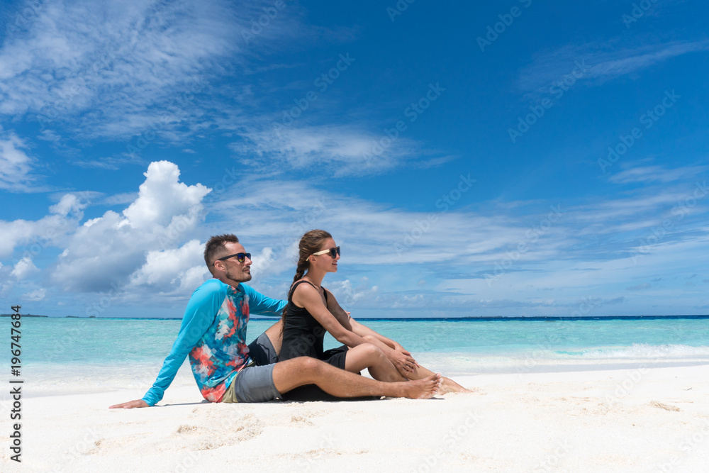 Man and woman sit on beach with transparent water of ocean in Maldives Man and woman sit on beach with transparent water of ocean in Maldives