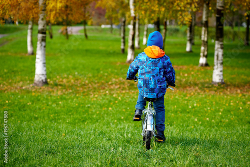 European boy is riding on the bicycle in the autumn city park. Back view.