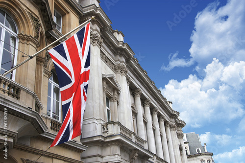 British Union Jack flag on a pole with buildings and a beautiful cloudy blue sky
