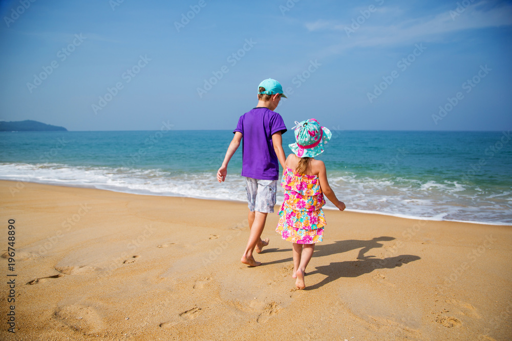 Мальчик и девочка держатся за руки и идут по песку к морю