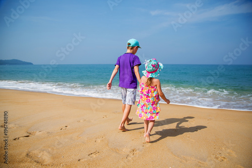 Мальчик и девочка держатся за руки и идут по песку к морю