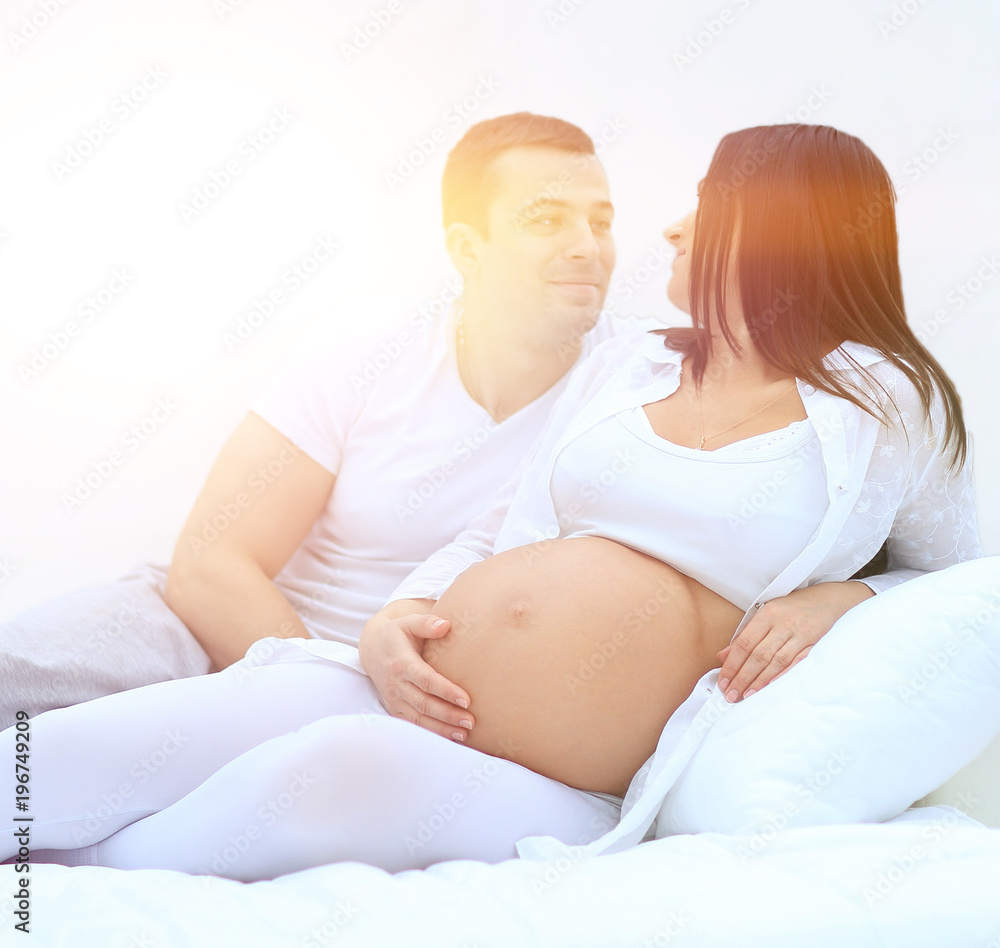 husband and pregnant wife lying on the bed in the bedroom. husband and pregnant wife lying on the bed in the bedroom.