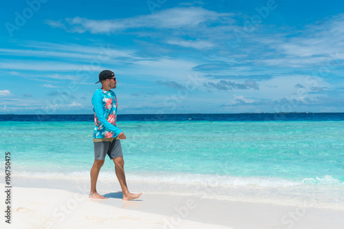 Man walking on beach with transparent water of ocean in Maldives