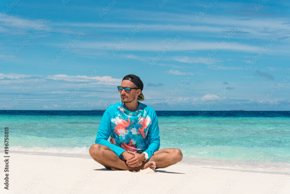 Man sit on sandy beach with transparent water of ocean in Maldives