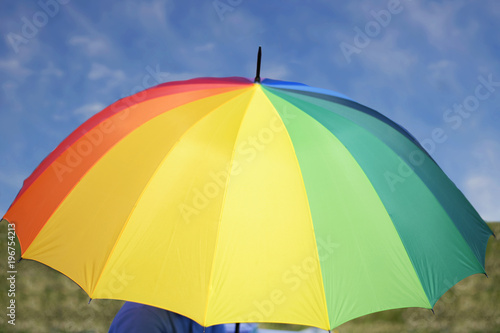 umbrella painted in rainbow colors closes a person against the background of a summer sky.