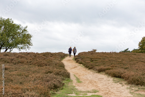 2 women walk up al hill on a sandy path at the Blaricummerheide.