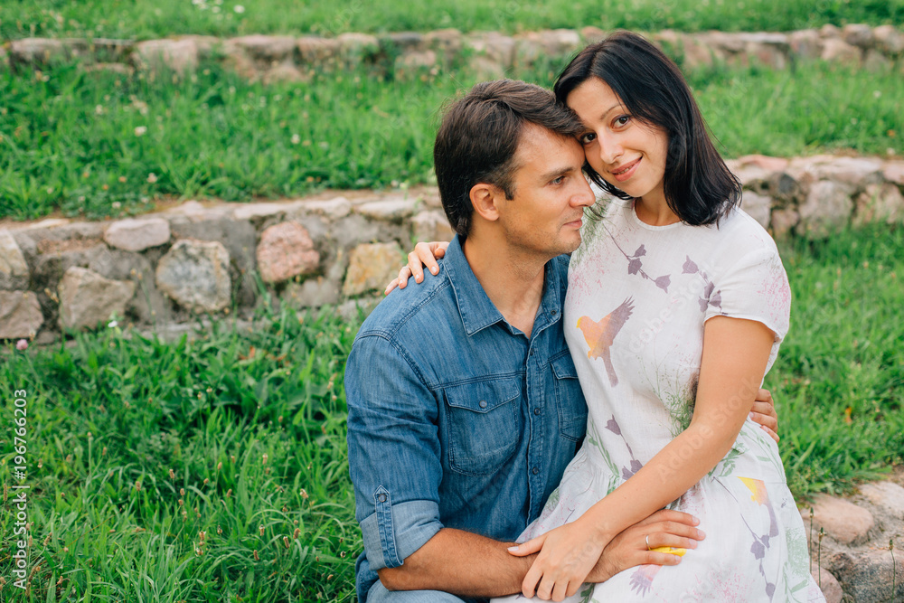 Pretty couple hugging and flirting in an urban park sitting on a stone bench and looking to each other. Man and woman having fun outdoors. Pretty couple hugging and flirting in an urban park sitting on a stone bench and looking to each other. Man and woman having fun outdoors.