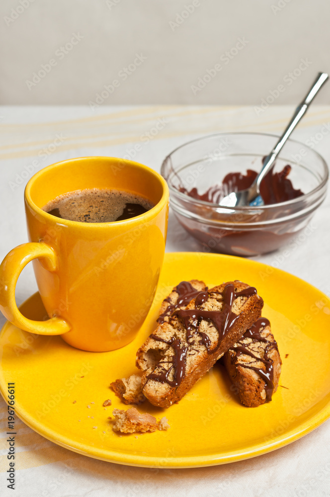 Top view of three, freshly baked, homemade, peanut butter oatmeal biscotti on a round, yellow plate with a large yellow cup of hot, coffee and a glass bowl of chocolate frosting Top view of three, freshly baked, homemade, peanut butter oatmeal biscotti on a round, yellow plate with a large yellow cup of hot, coffee and a glass bowl of chocolate frosting