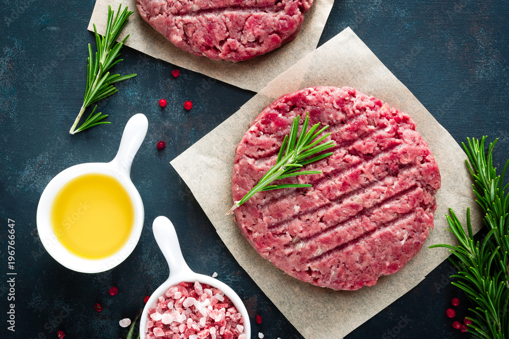 Fresh minced beef meat burgers with spices on dark background. Raw ground beef meat. Flat lay. Top view Fresh minced beef meat burgers with spices on dark background. Raw ground beef meat. Flat lay. Top view