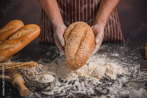 Man preparing buns at table in bakery, Man sprinkling flour over fresh dough on kitchen table