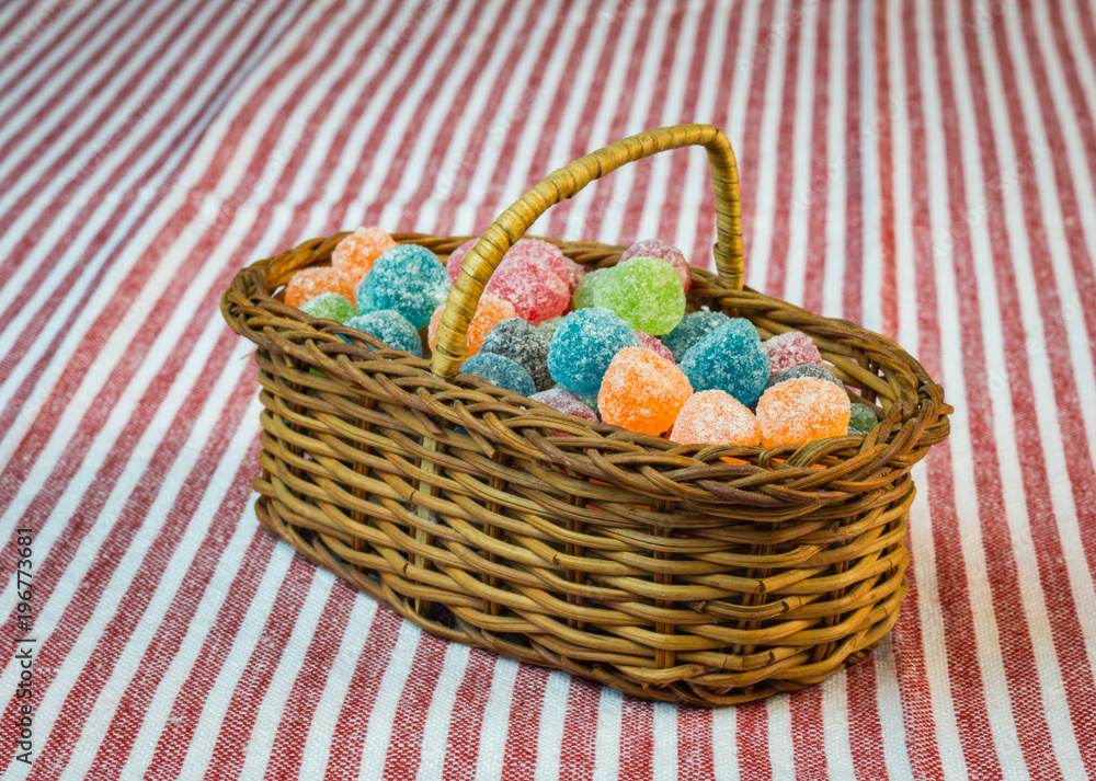 Sugar coated jelly sweets in wicker basket on striped tablecloth Sugar coated jelly sweets in wicker basket on striped tablecloth