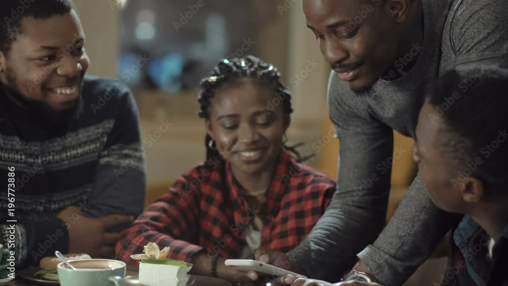 Group of laughing African-American men and girl watching something on smartphone and laughing while chilling in cafe. Group of laughing African-American men and girl watching something on smartphone and laughing while chilling in cafe.