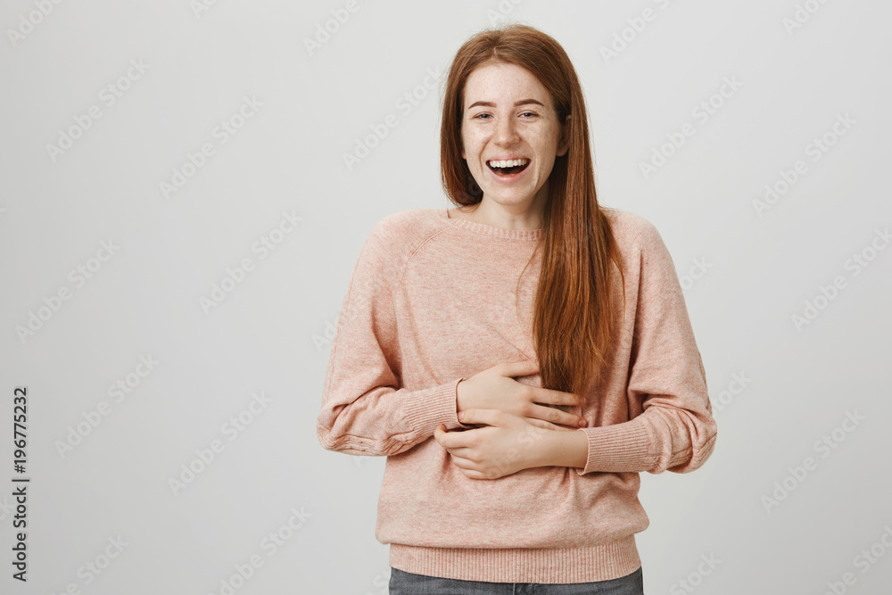 Portrait of cute charming ginger woman laughing loudly and holding belly with hands because of pain in muscles, standing over gray background. I literally can not remember joke better than this one Portrait of cute charming ginger woman laughing loudly and holding belly with hands because of pain in muscles, standing over gray background. I literally can not remember joke better than this one