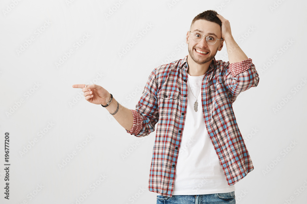 Confused embarrassed attractive man in glasses pointing left while holding hand on head, looking surprised and awkward, smiling at camera. Guy forgot name of his coworker and asks friend to help him Confused embarrassed attractive man in glasses pointing left while holding hand on head, looking surprised and awkward, smiling at camera. Guy forgot name of his coworker and asks friend to help him