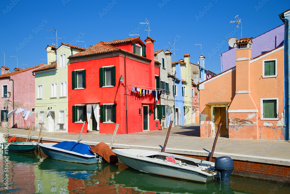 Red house on the embankment of the city channel. Sunny day on the Burano island, Venice