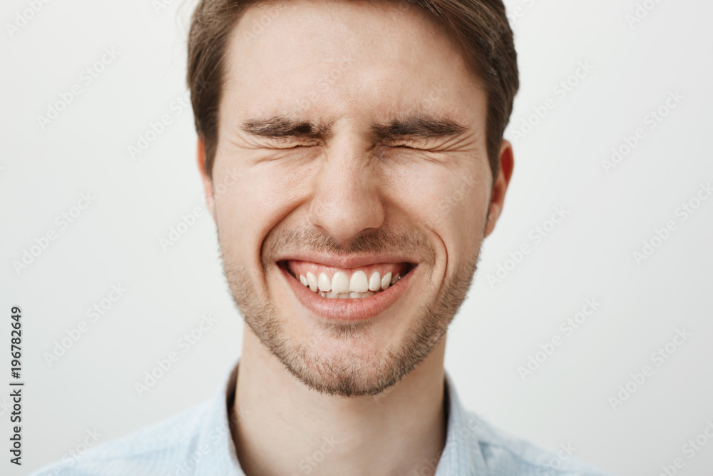 Emotive happy european guy with bristle standing with tightly closed eyes, squinting and smiling broadly, waiting for surprise or making wish near birthday cake, standing over gray background Emotive happy european guy with bristle standing with tightly closed eyes, squinting and smiling broadly, waiting for surprise or making wish near birthday cake, standing over gray background